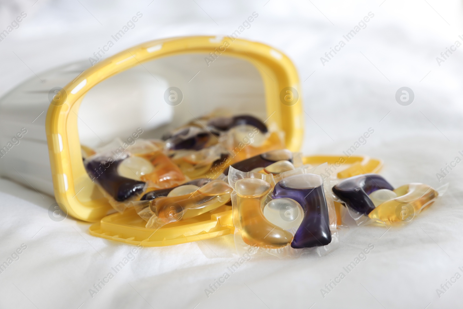 Photo of Laundry detergent capsules in container on white fabric, closeup