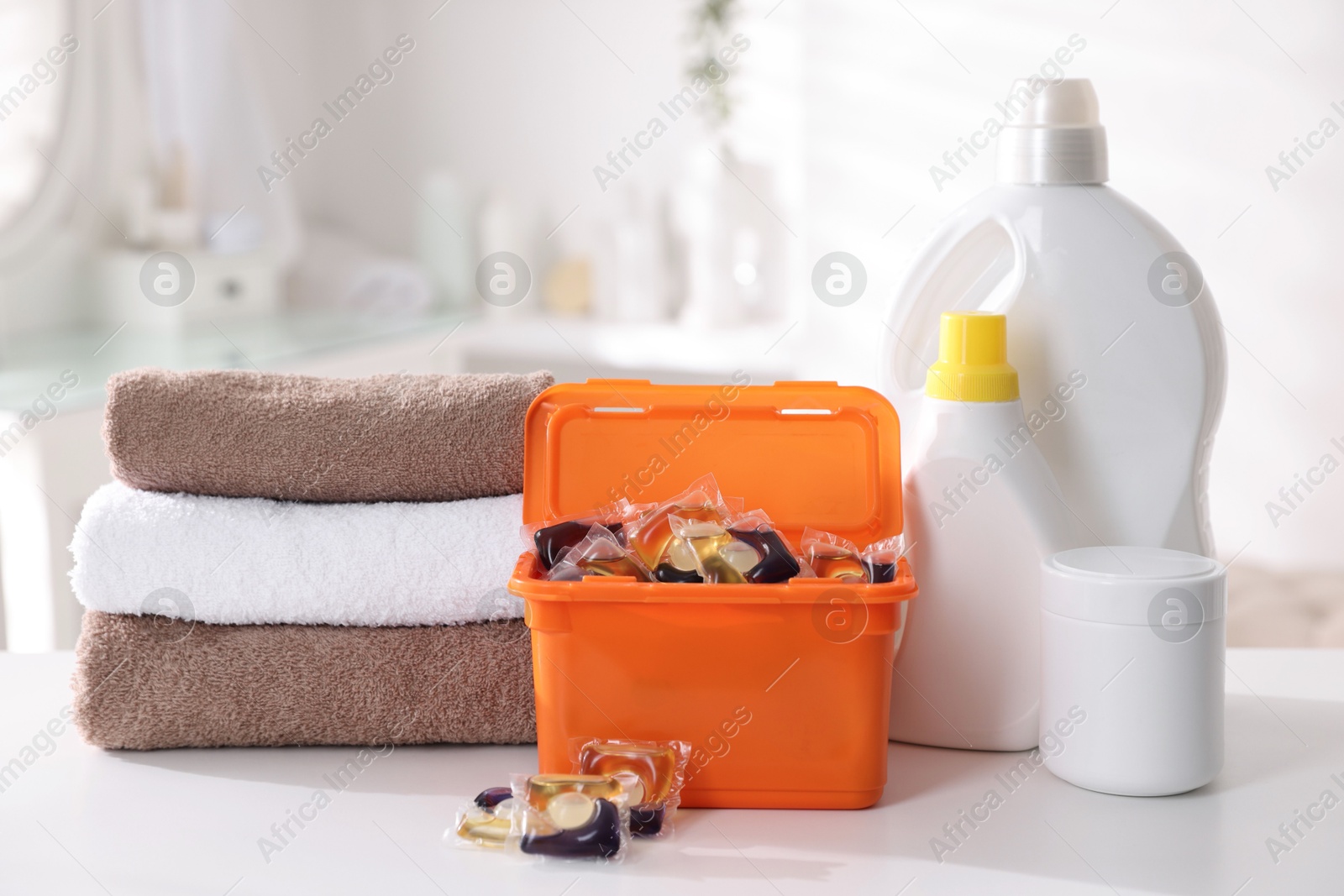 Photo of Laundry capsules, detergents and clean towels on white table in bathroom