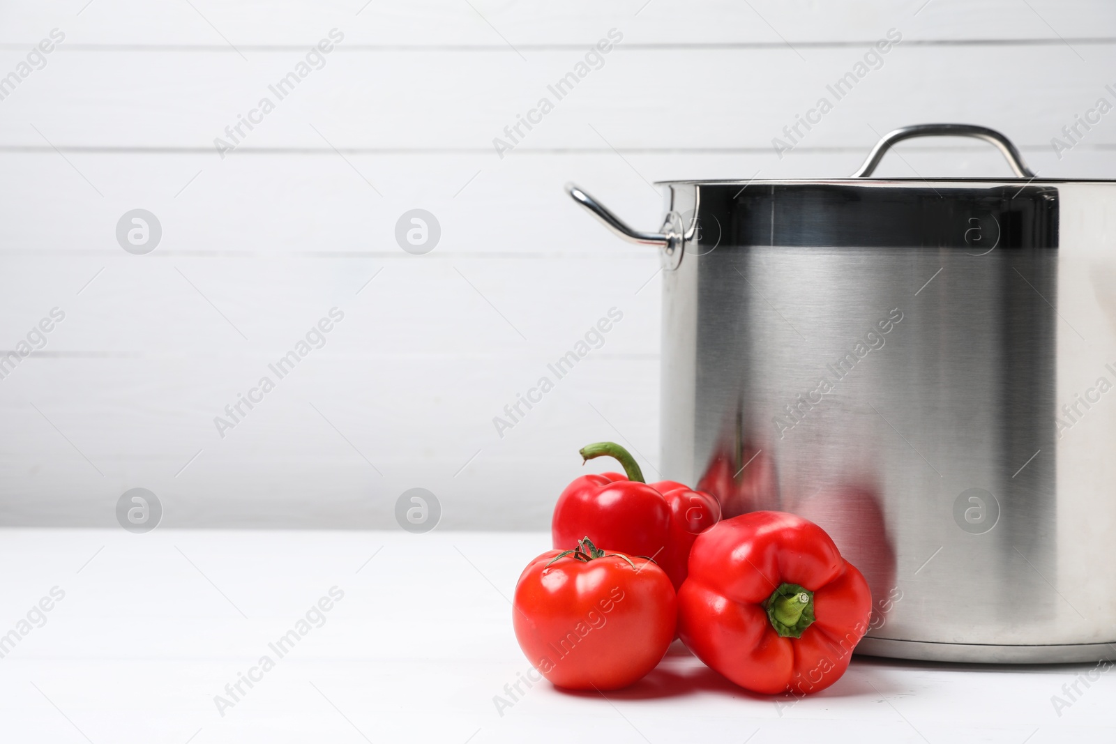 Photo of Stainless steel pot and vegetables on white table, space for text