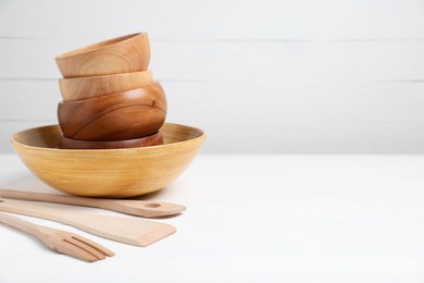 Photo of Wooden bowls and cooking utensils on white table, space for text