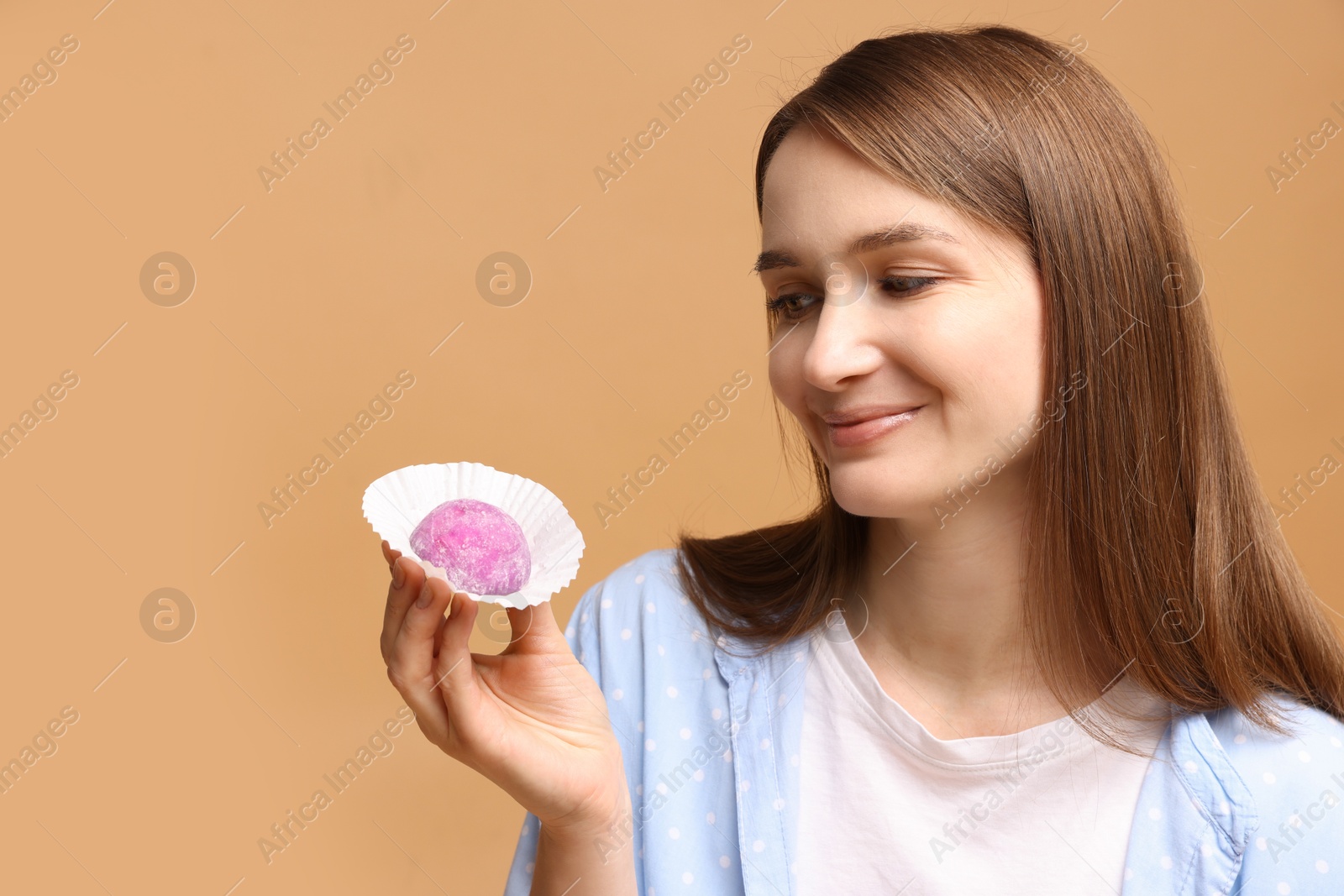 Photo of Woman with tasty mochi on light brown background. Space for text