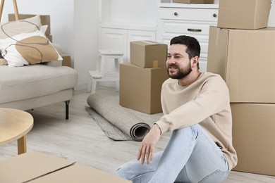 Photo of Moving day. Man resting on floor near cardboard boxes in his new home