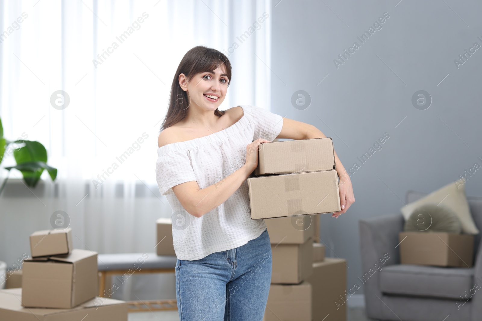 Photo of Moving day. Happy woman with cardboard boxes in her new home