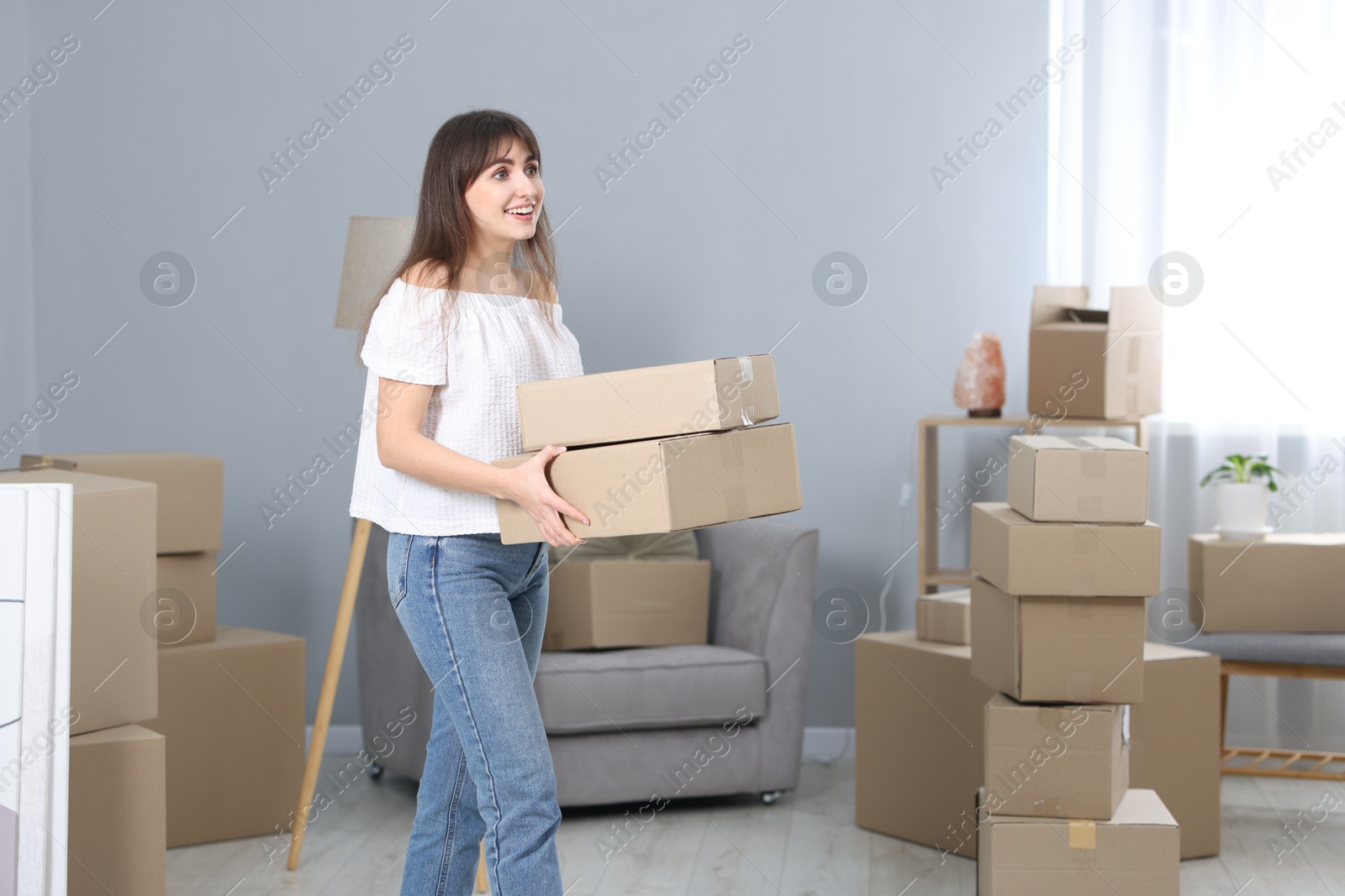 Photo of Moving day. Happy woman with cardboard boxes in her new home