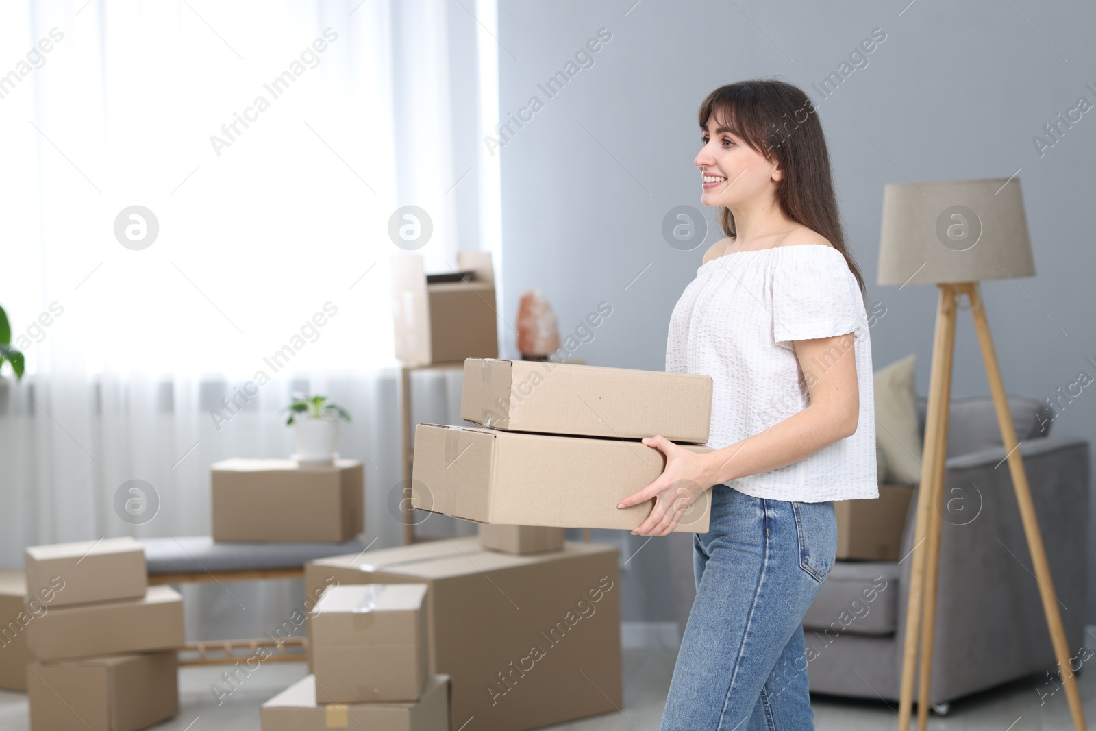 Photo of Moving day. Happy woman with cardboard boxes in her new home