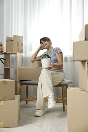 Moving day. Happy woman with houseplant and cardboard boxes in her new home