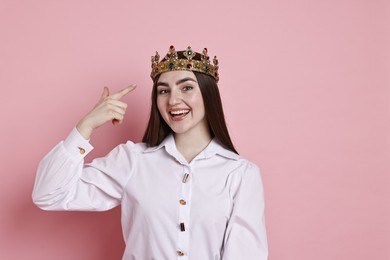 Photo of Happy woman pointing at elegant crown on pink background. Space for text