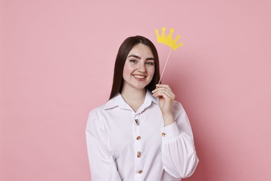 Photo of Happy woman holding stick with paper crown on pink background