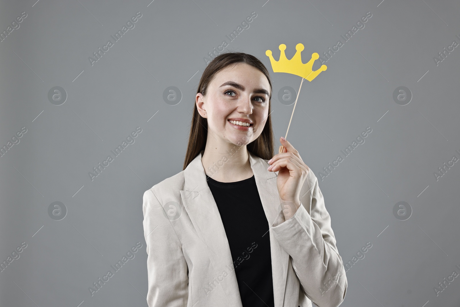 Photo of Smiling businesswoman holding stick with paper crown on grey background