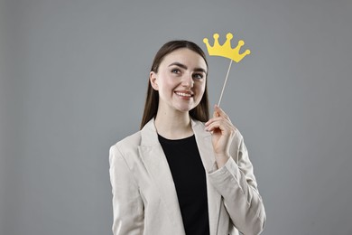 Photo of Smiling businesswoman holding stick with paper crown on grey background