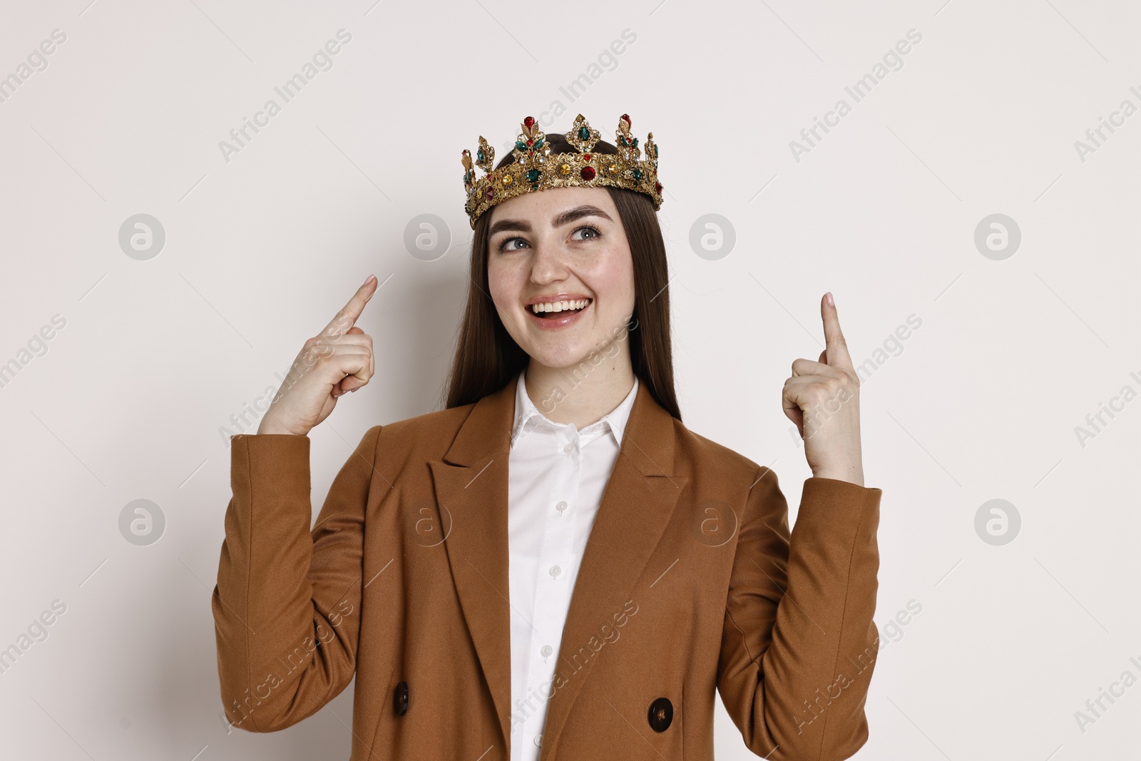 Photo of Happy businesswoman in elegant crown pointing upwards on light background