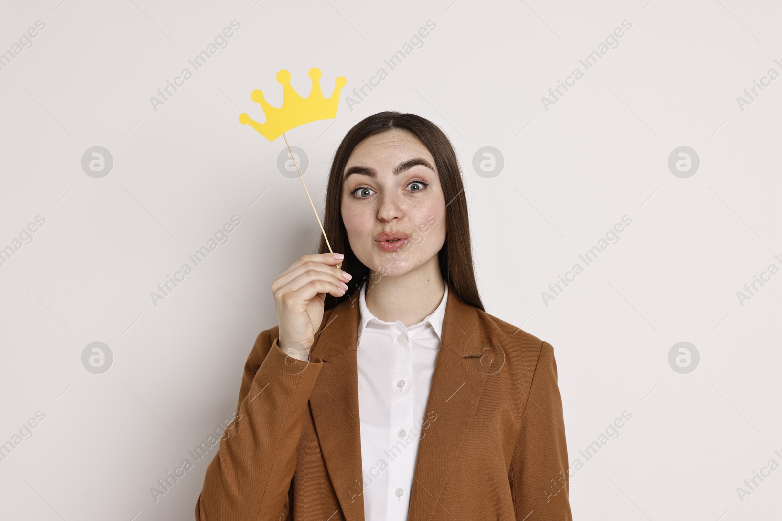 Photo of Emotional businesswoman holding stick with paper crown on light background