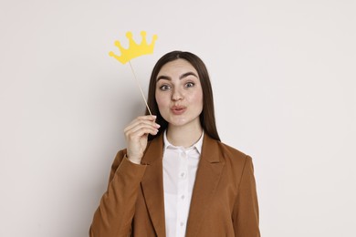 Photo of Emotional businesswoman holding stick with paper crown on light background