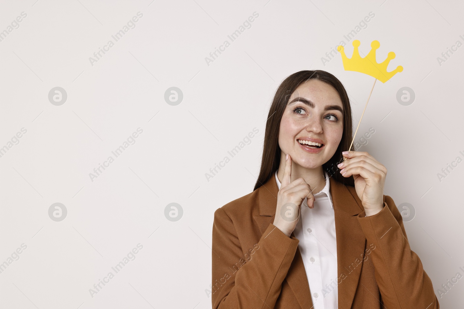 Photo of Happy businesswoman holding stick with paper crown on light background. Space for text