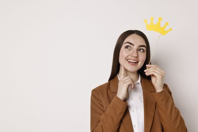 Photo of Happy businesswoman holding stick with paper crown on light background. Space for text