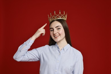 Photo of Smiling woman pointing at elegant crown on dark red background