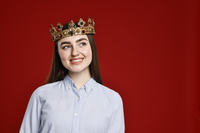 Photo of Smiling woman in elegant crown on dark red background. Space for text