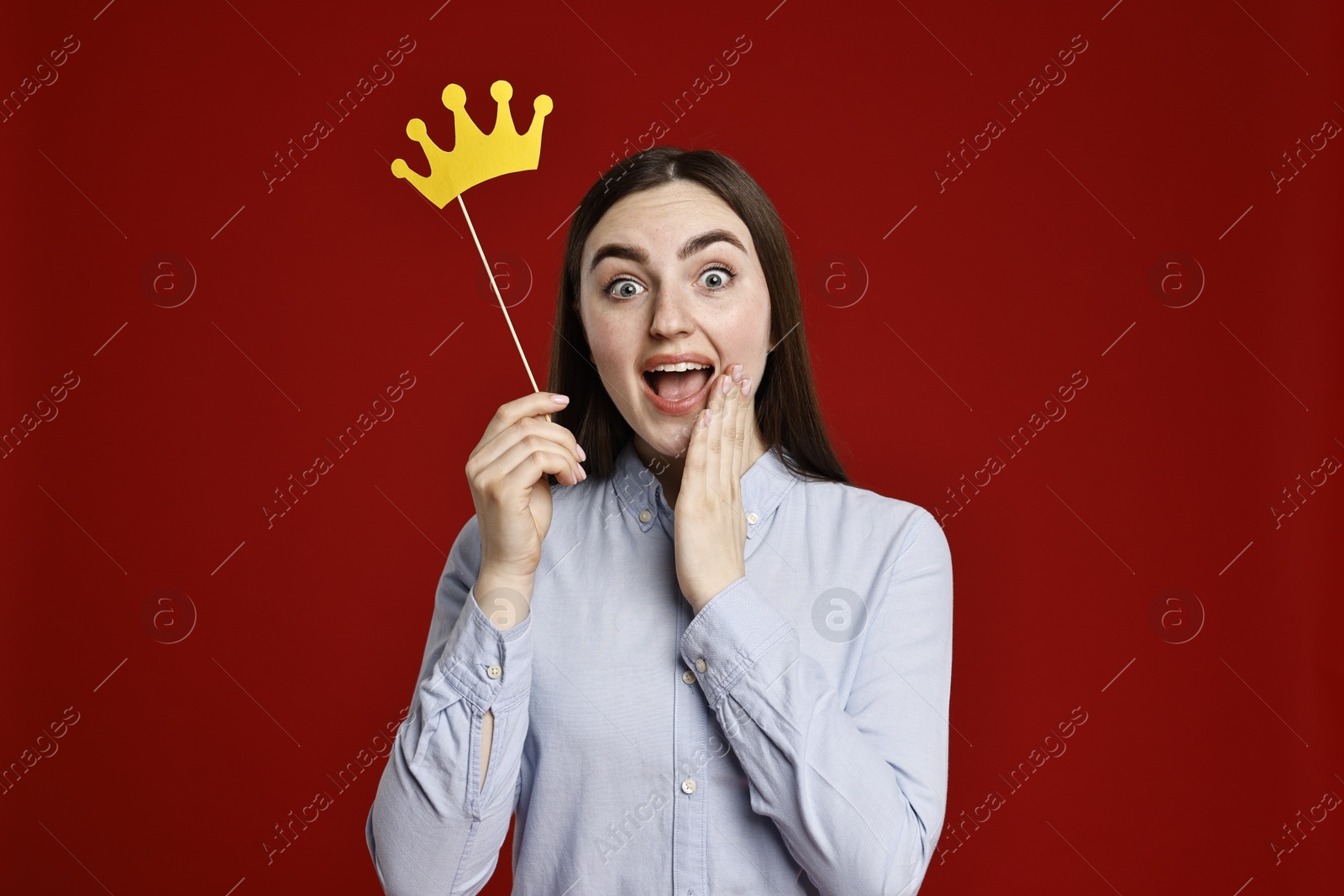 Photo of Emotional woman holding stick with paper crown on dark red background