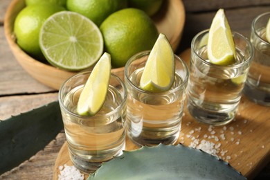 Photo of Tequila shots with lime slices, salt and agave leaves on wooden table, closeup