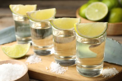 Photo of Tequila shots with lime slices, salt and agave leaves on wooden table, closeup