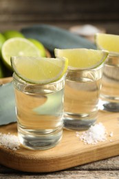 Photo of Tequila shots with lime slices, salt and agave leaves on wooden table, closeup