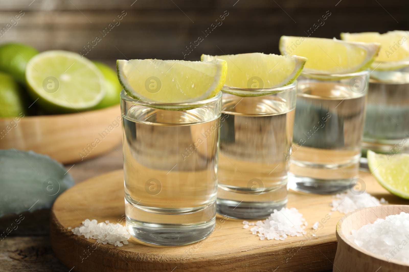 Photo of Tequila shots with lime slices, salt and agave leaf on wooden table, closeup