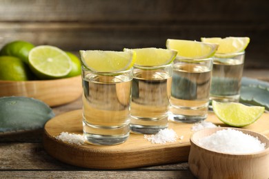 Photo of Tequila shots with lime slices, salt and agave leaves on wooden table, closeup