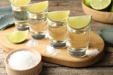 Photo of Tequila shots with lime slices, salt and agave leaves on wooden table, closeup