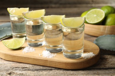 Photo of Tequila shots with lime slices, salt and agave leaves on wooden table, closeup