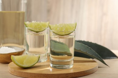 Photo of Tequila shots with lime slices, salt and agave leaves on wooden table