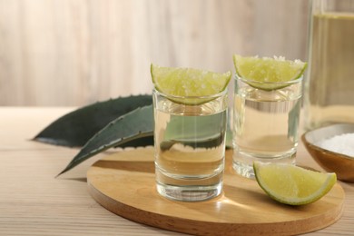 Photo of Tequila shots with lime slices, salt and agave leaves on wooden table. Space for text