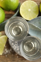 Photo of Tequila shots with salt, limes and agave leaves on wooden table, flat lay