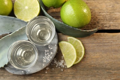 Photo of Tequila shots with salt, limes and agave leaves on wooden table, flat lay