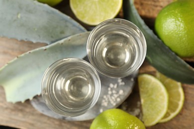 Photo of Tequila shots with salt, limes and agave leaves on wooden table, flat lay