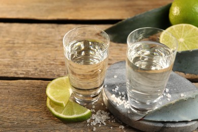 Photo of Tequila shots with salt, limes and agave leaves on wooden table, closeup