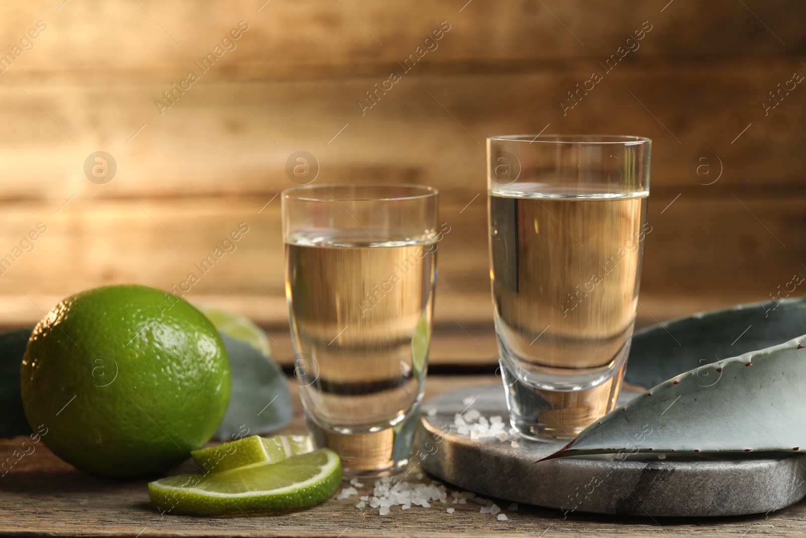 Photo of Tequila shots with salt, limes and agave leaves on table