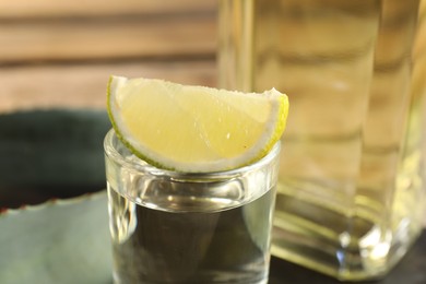 Photo of Tequila shot with lime slice and agave leaves on table, closeup