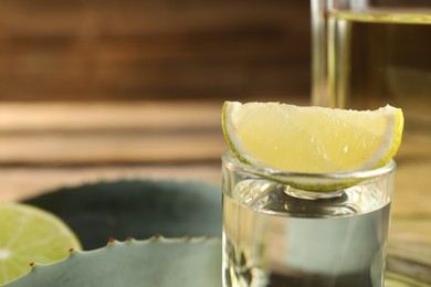 Photo of Tequila shot with lime slice and agave leaves on table, closeup. Space for text