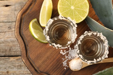 Photo of Tequila shots with salt, lime slices and agave leaves on wooden table, flat lay