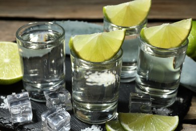 Tequila shots with lime slices, salt, ice cubes and agave leaf on table, closeup