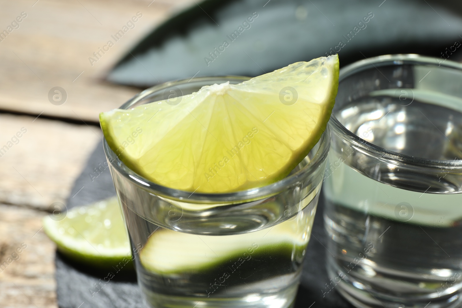 Photo of Tequila shots with lime slice on wooden table, closeup