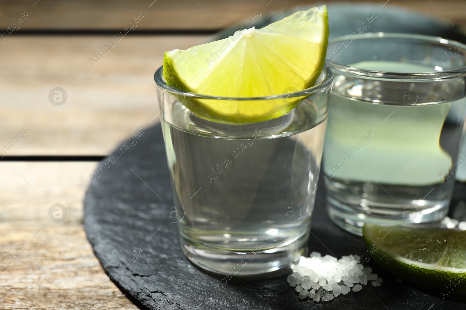 Photo of Tequila shots with lime slice and salt on wooden table, closeup