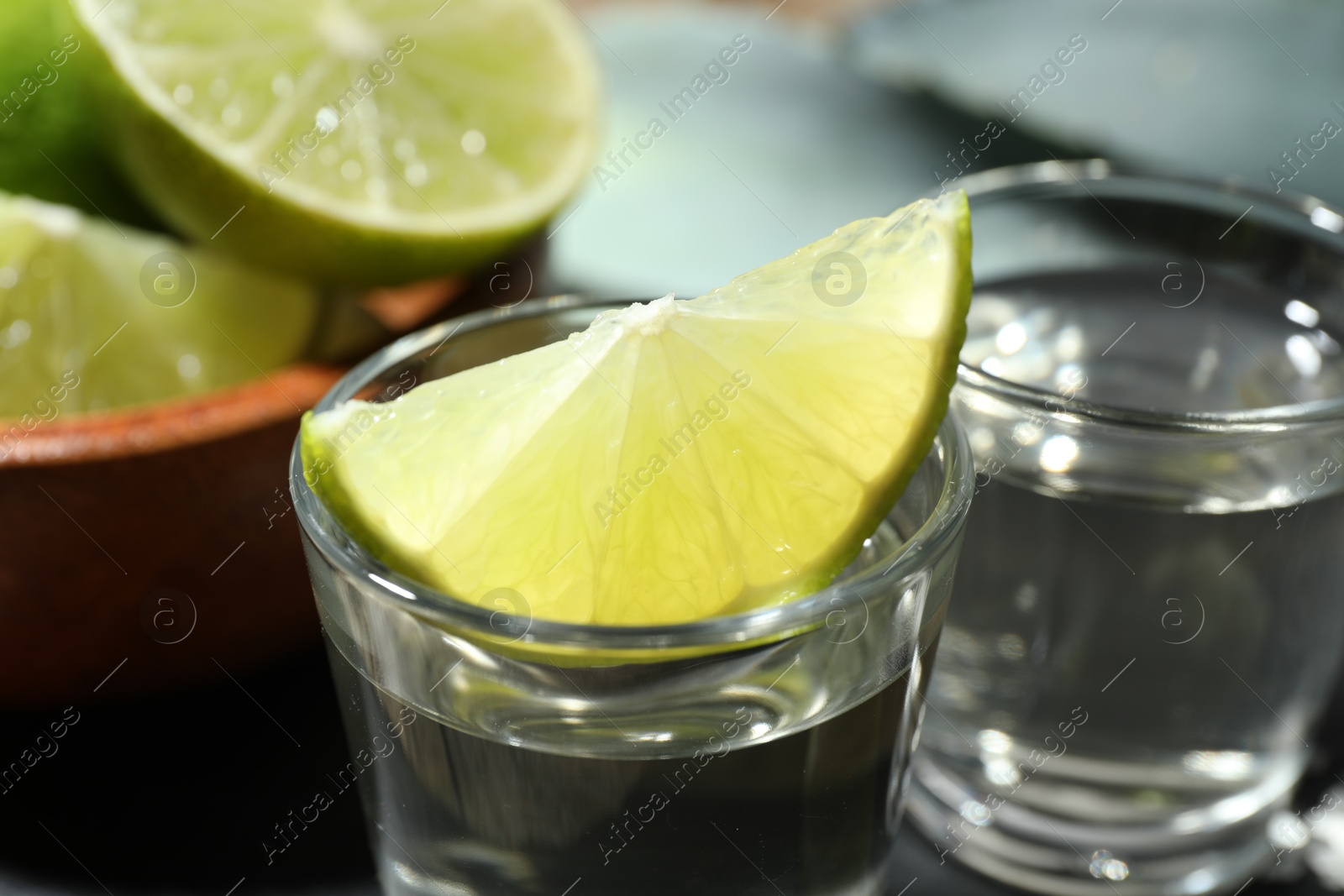 Photo of Tequila shots with lime slices on table, closeup