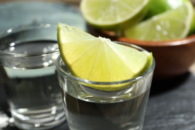 Photo of Tequila shots with lime slices on table, closeup