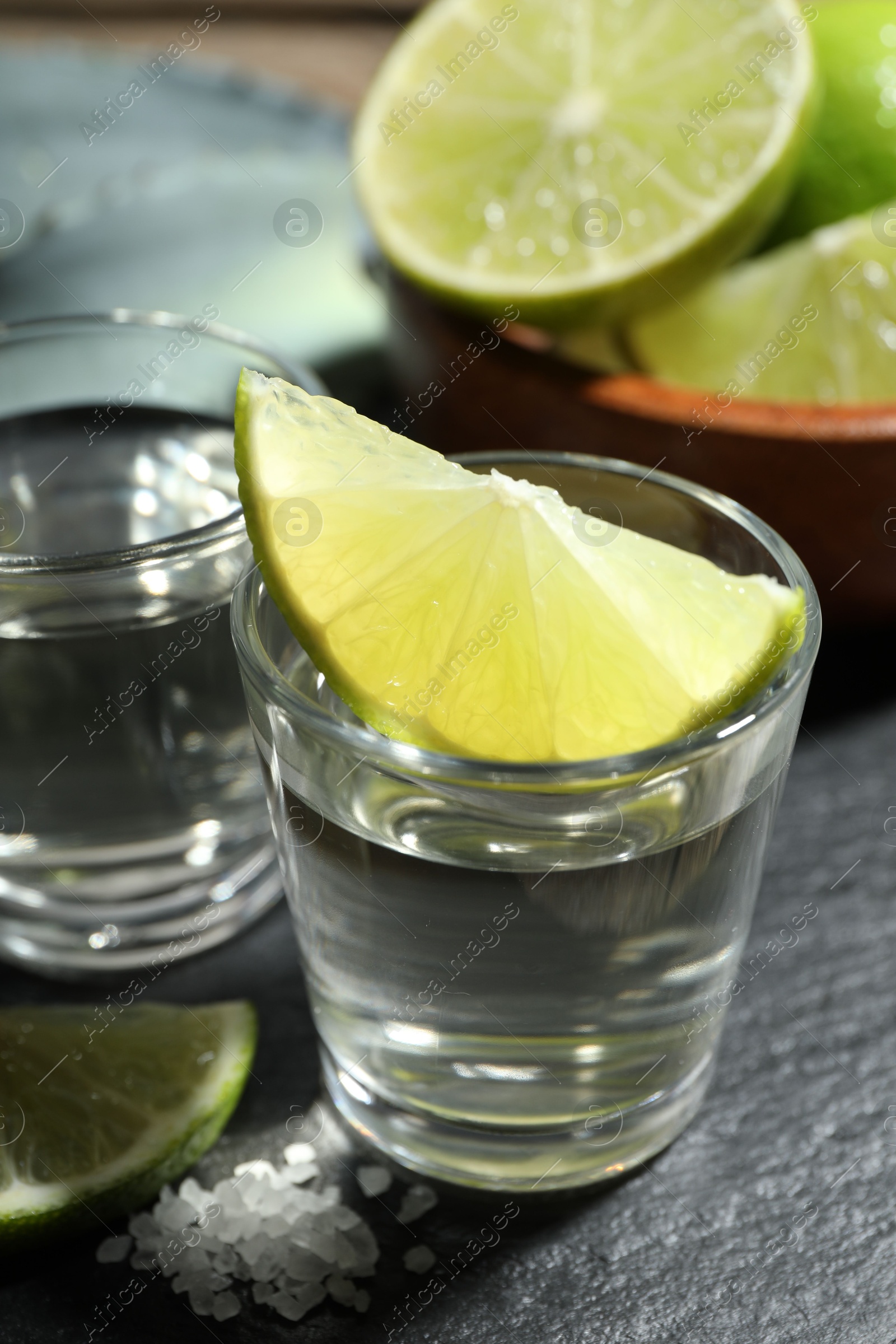 Photo of Tequila shots with lime slices and agave leaves on table, closeup