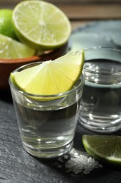 Photo of Tequila shots with lime slices and agave leaves on table, closeup