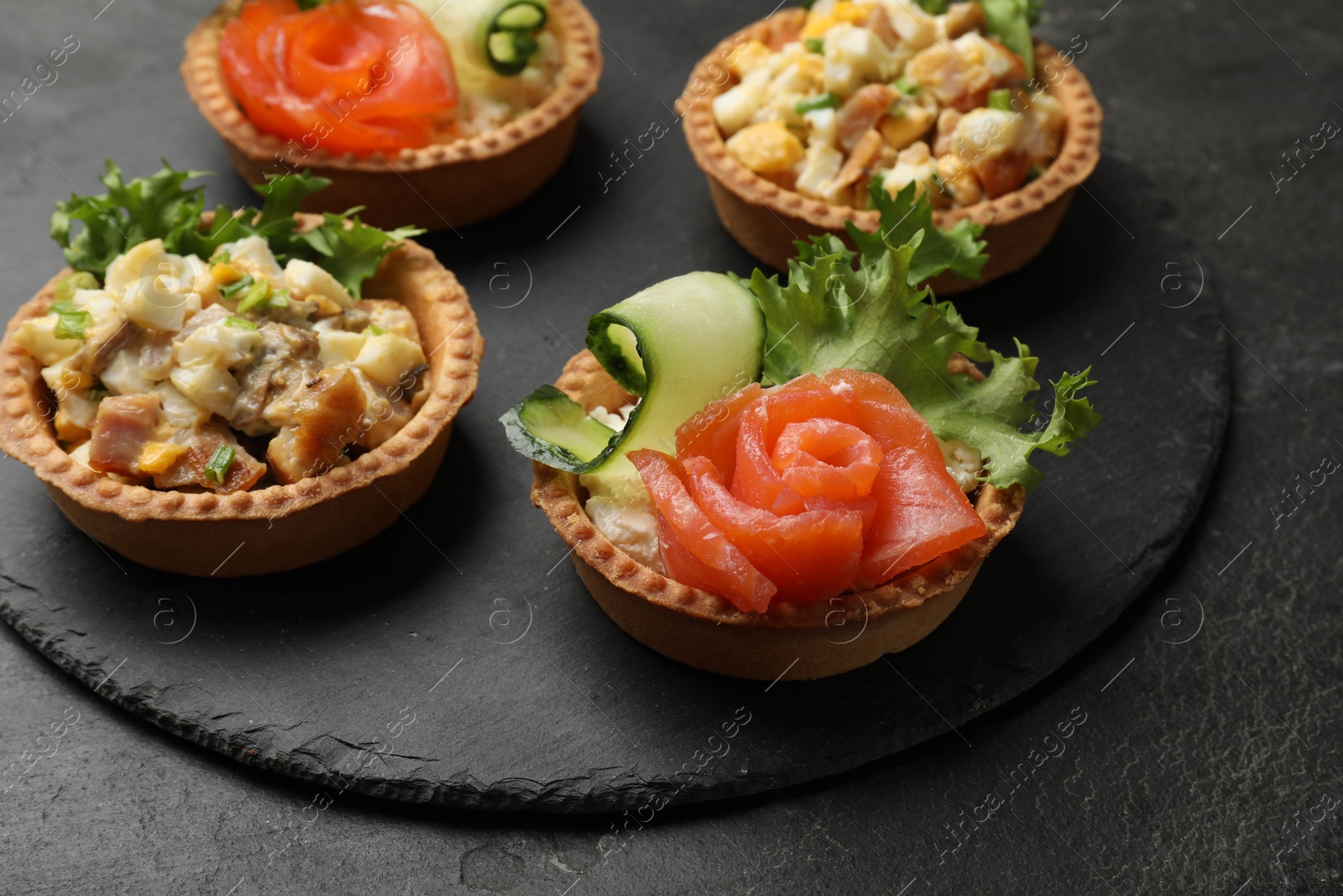 Photo of Tartlets with delicious fillings on black table, closeup