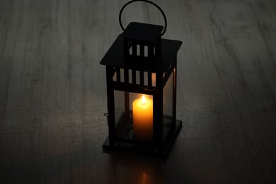 Photo of Beautiful lantern with burning candle on dark wooden surface