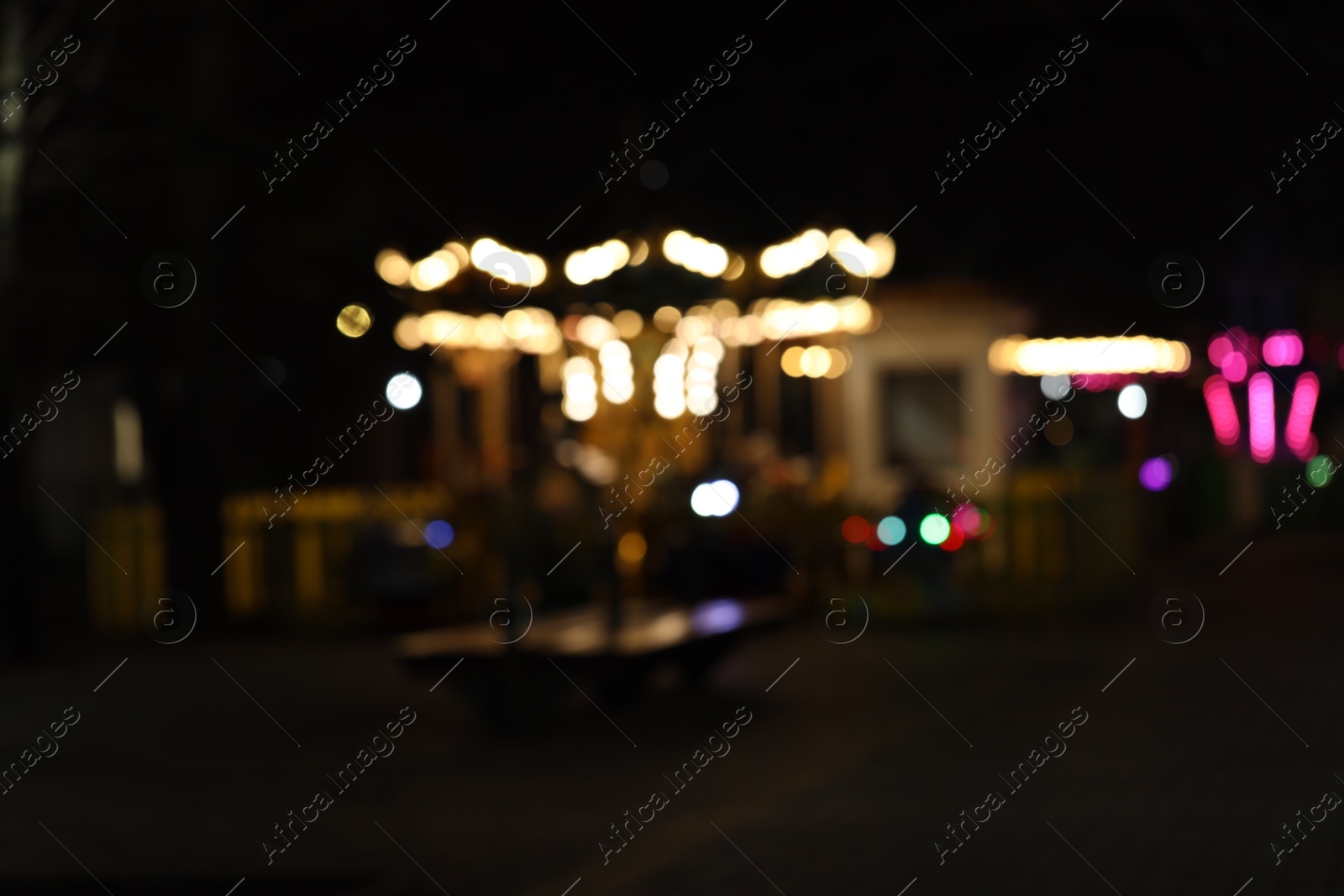 Photo of Blurred view of city street with illuminated rides at night