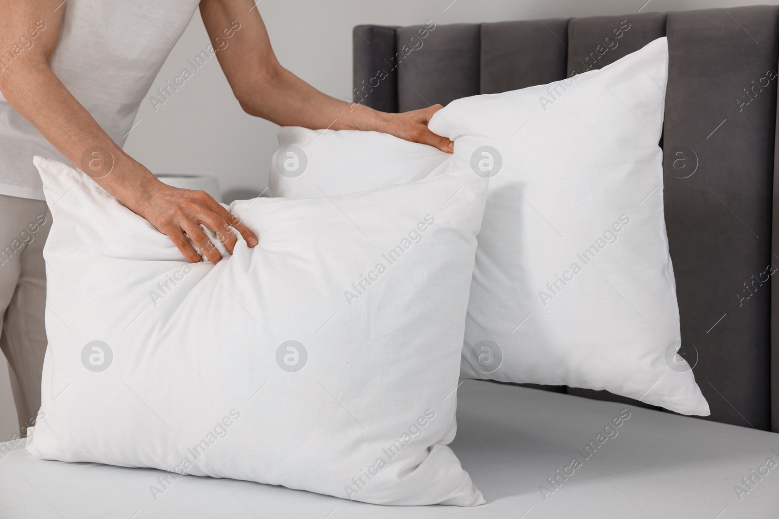 Photo of Woman putting pillows on bed at home, closeup. Space for text